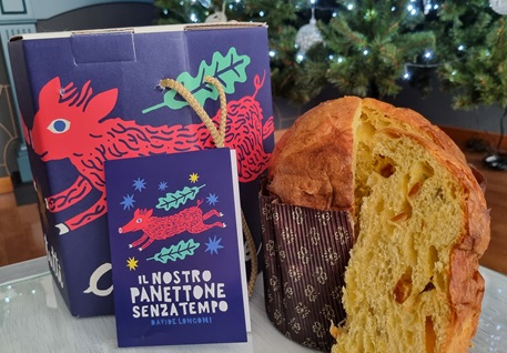 Panettone con una fetta tagliata in primo piano e confezione in cartone con disegni viola e rossi 
